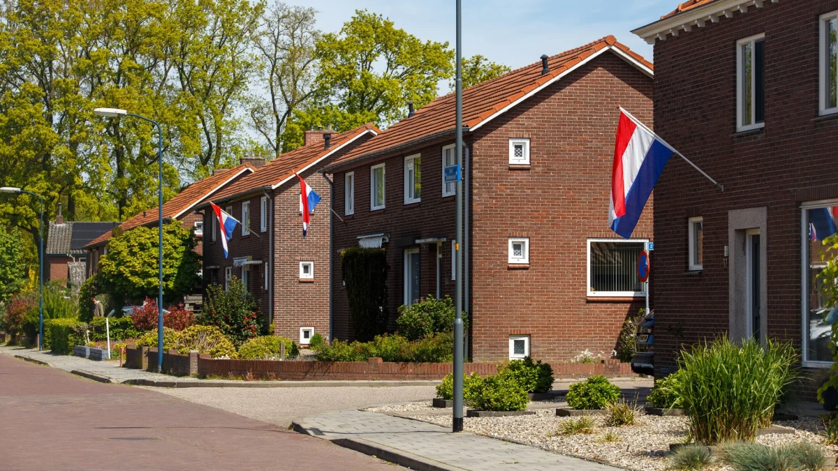 Een pittoreske straat in een buitenwijk van Nederland met Nederlandse vlaggen die op een zonnige dag aan bakstenen huizen wapperen.