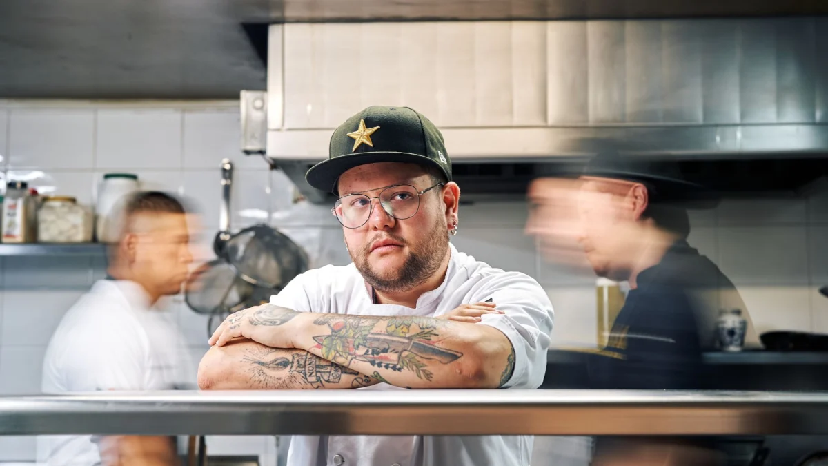 Een zelfverzekerde chef-kok staat in een drukke restaurantkeuken, omringd door een dynamische, wazige omgeving.