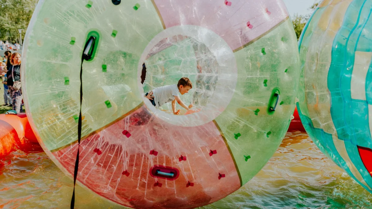 Een kind speelt graag in een vrolijke, opblaasbare waterbal op een buitenkermis.