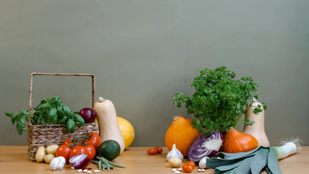 Een verscheidenheid aan verse groenten, waaronder pompoen, tomaten en bladgroenten, gerangschikt op een houten tafel.